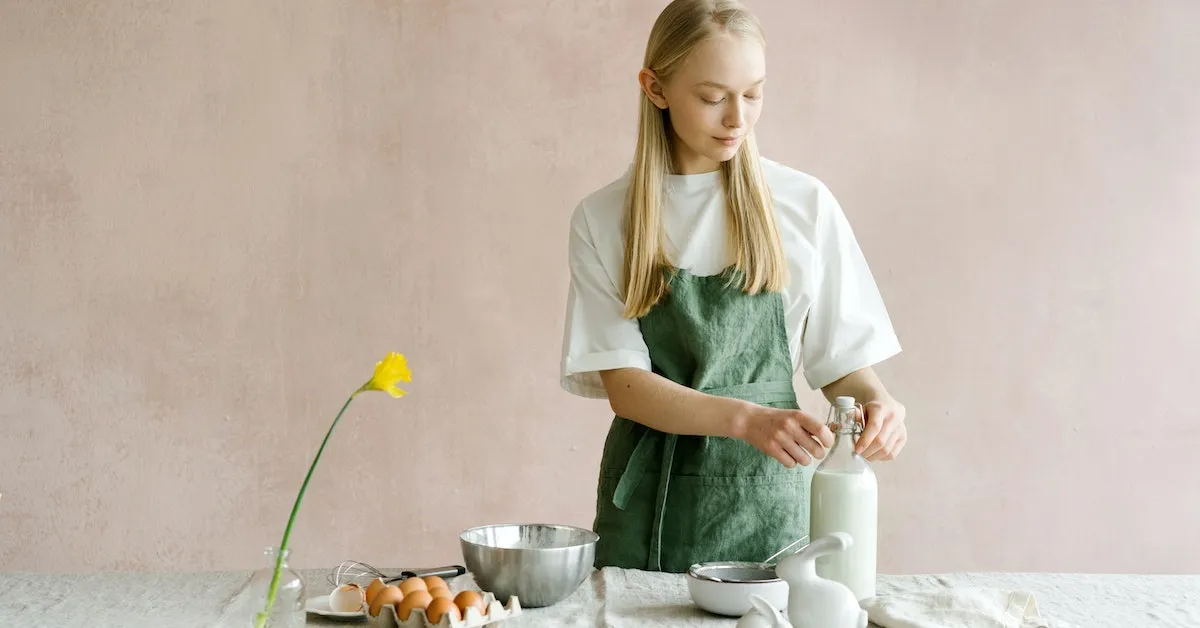 A woman wearing an apron standing in front of a table with a flower, eggs, milk, and cheese. Learn how to save your food from going bad so quickly in our latest article.