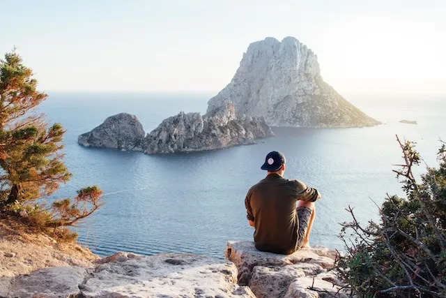 A man sitting in front of an ocean with large rocky islands. Learn how to enjoy life and find peace through our topics here at Ads4Dads.com