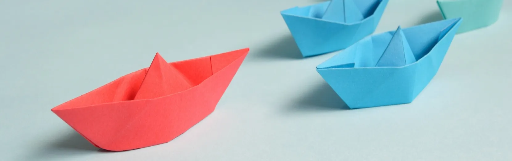 A small handmade paper boat that is red in color, it is leading three other smaller blue boats. Our category of Leadership found at Ads4Dads.com