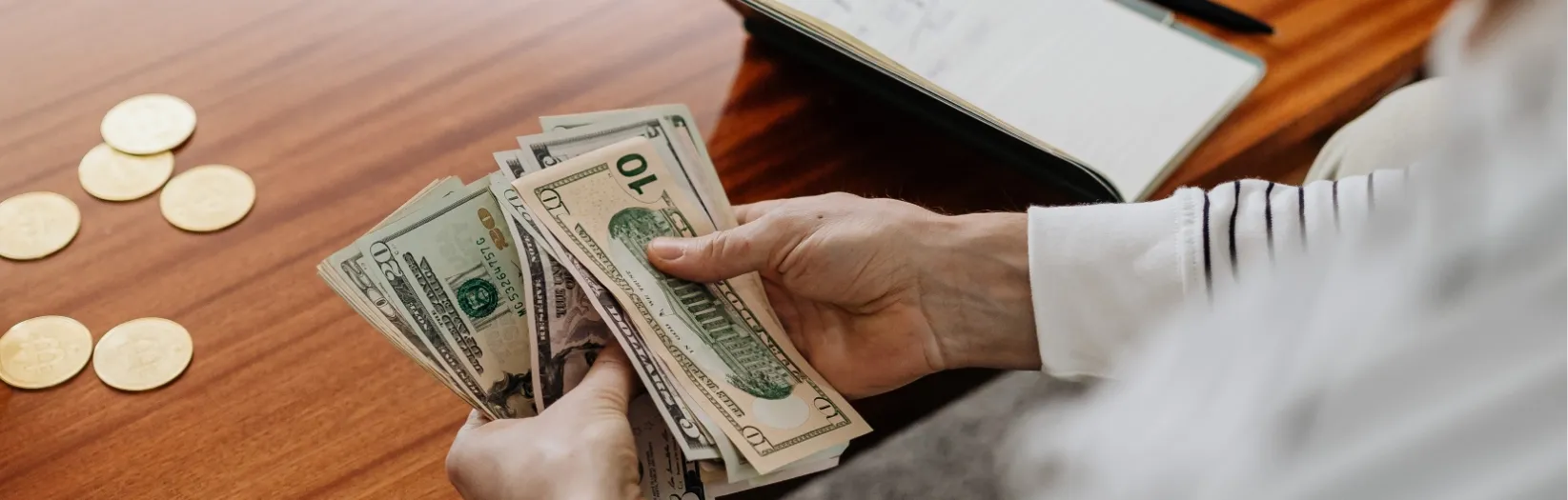 A person counting American paper currency with a couple of coins laying on the table in front. Our category of Money Saving Ideas found at Ads4Dads.com