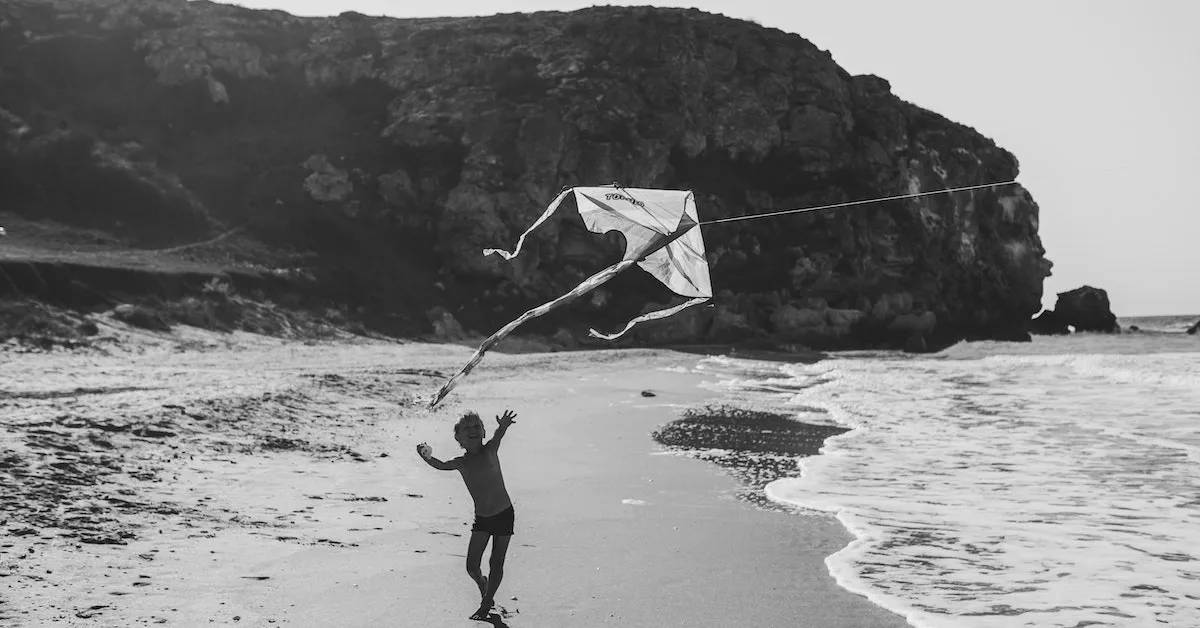 A young boy running along a beach holding a kite. Learn how to chase your dreams in this latest article from Ads4dads.com