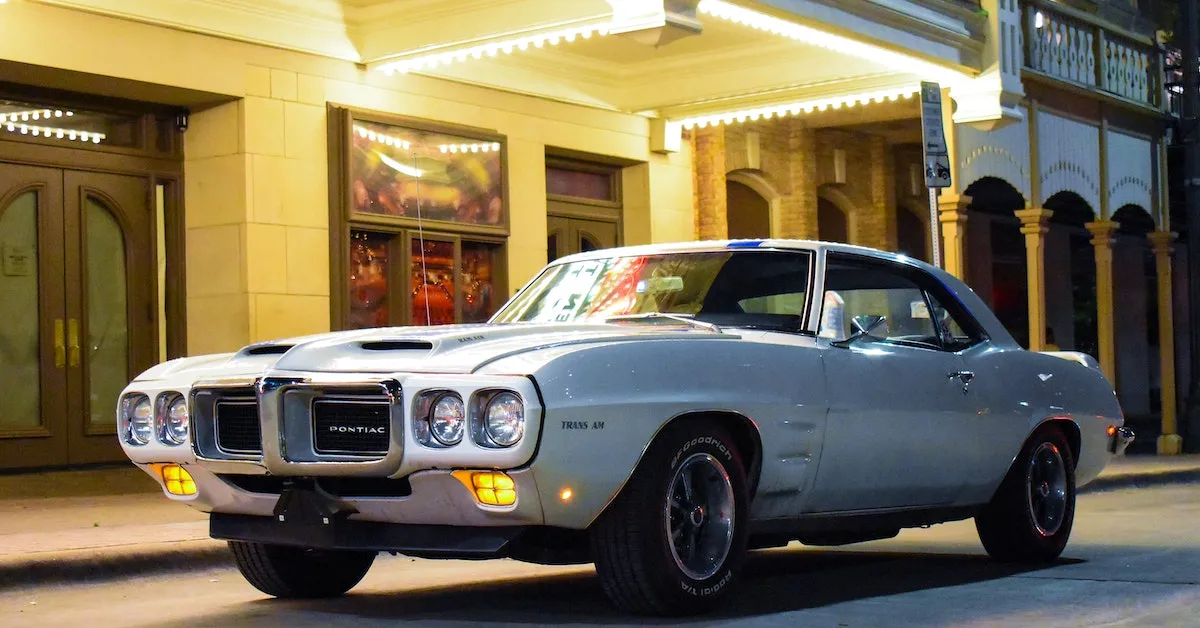 A light blue1968 Pontiac Trans Am hardtop. The background is an old movie theatre. Read about this cool story found in our latest article here at Ads4Dads.com