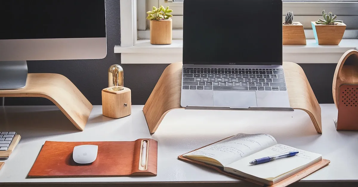 An Apple desktop computer next to an Apple laptop. On the desk is an open note pad and a pen to take notes and learn. Let's talk about the benefit of day trading today. -Ads4dads.com