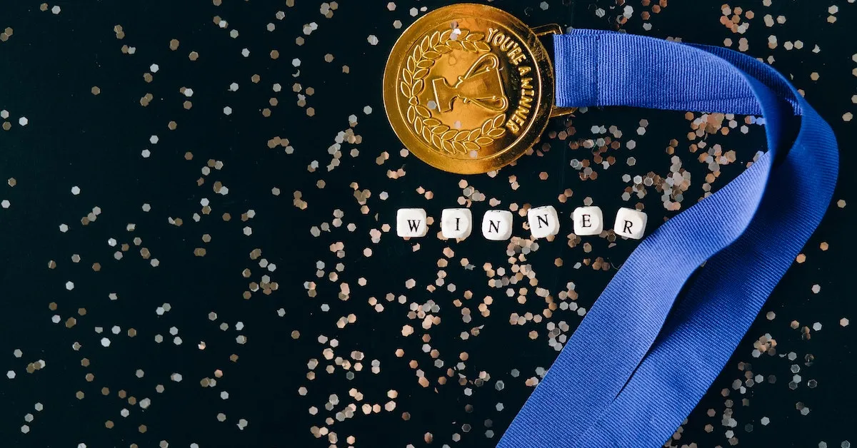 A gold medal with a blue ribbon, there is confetti in the background with the word "winner" spelled out. Learn about the healthy rewards found in your health insurance and the benefits available to you.