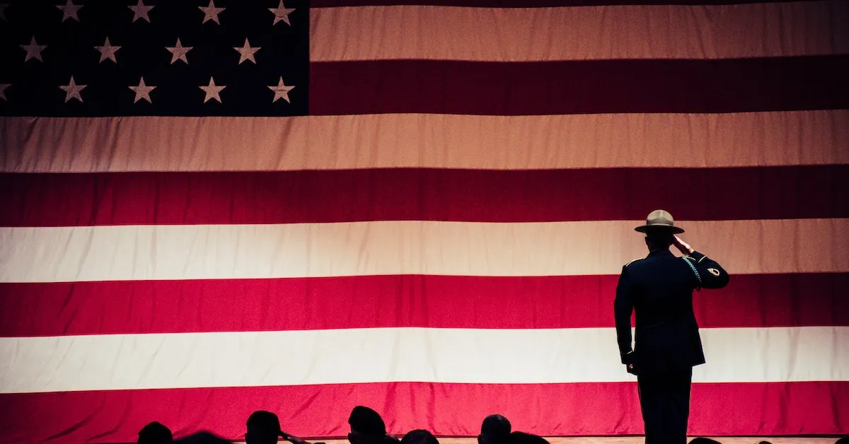 An American soldier saluting a very large American flag. There is also many people in the foreground. Find reasons to pursue leadership and the information you need to be successful in our latest article. -Ads4Dads.com