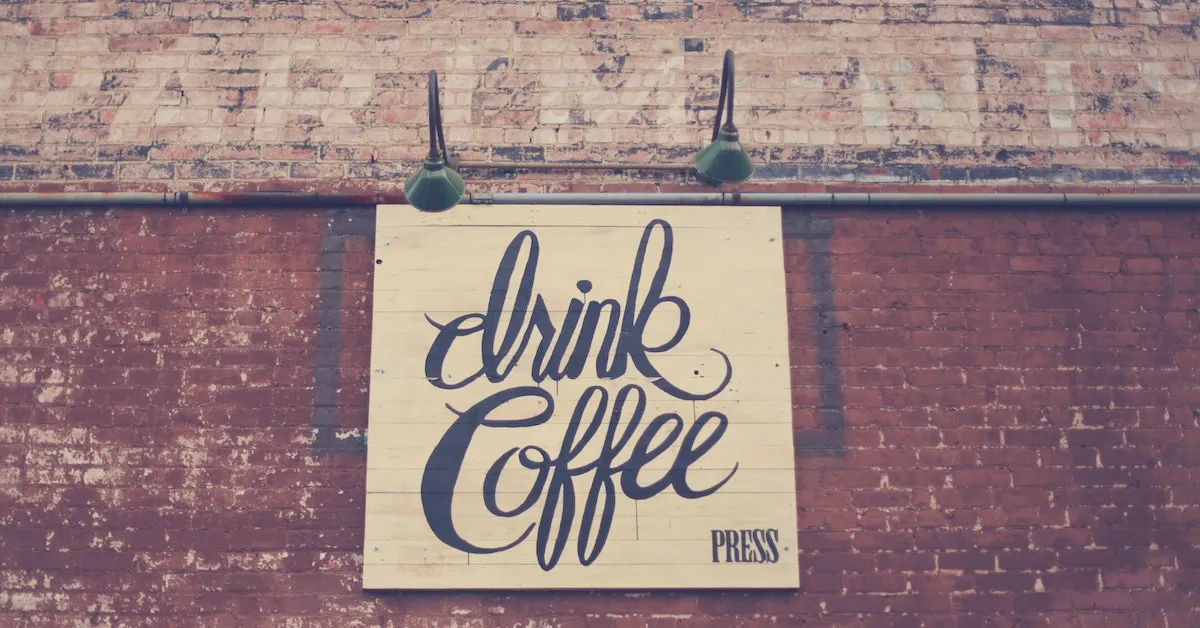 a large sign mounted to a brick wall that reads: "drink coffee" in cursive letters. Find out why coffee and caffeine may not be beneficial for us neurologically.