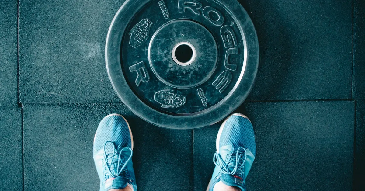 A large gym weight made by Rogue and someone standing just above it, all you see is their shoes. Learn some great time for the gym in this article.