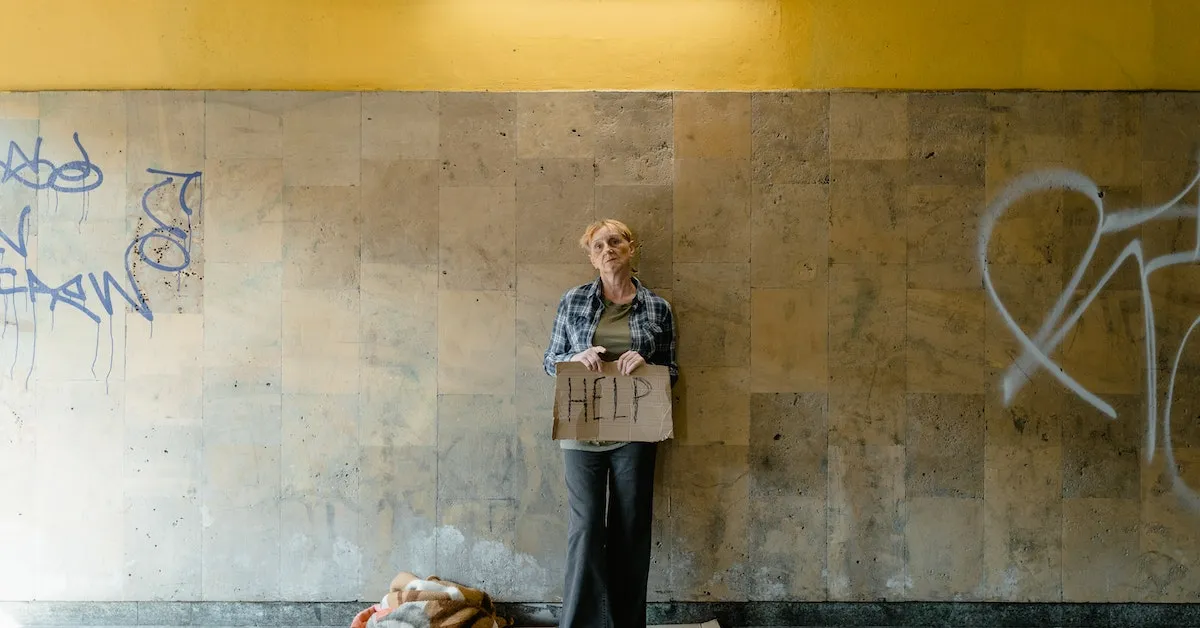 A homeless woman holding a cardboard sign that reads "help". Learn a better way to help the homeless in your area.