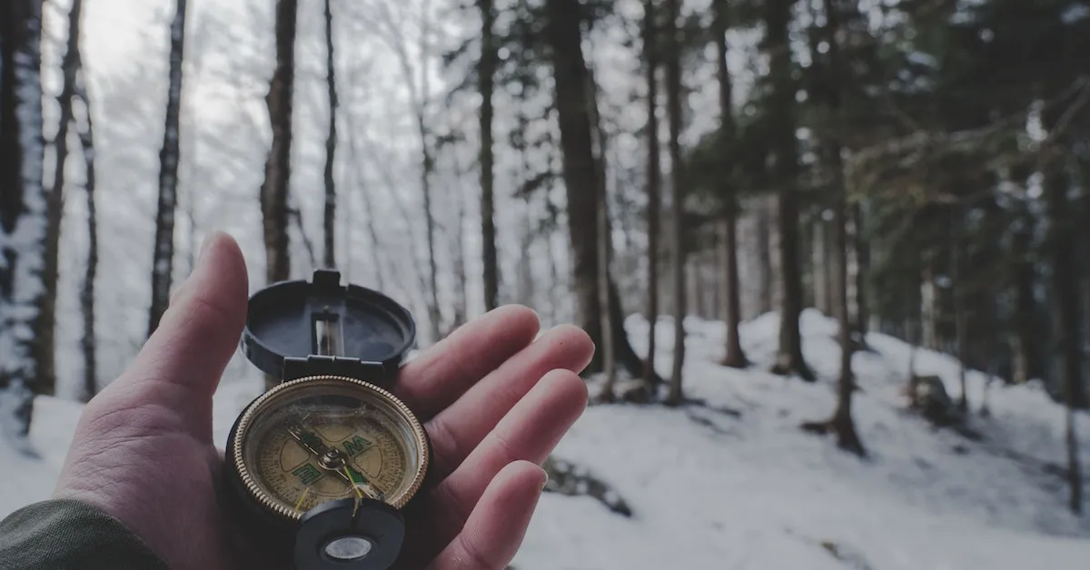 Someone holding an old compass in their left hand. The background is a wooded area on a snowy day. You'll find a lot of resources to navigate to here on Ads4Dads.com