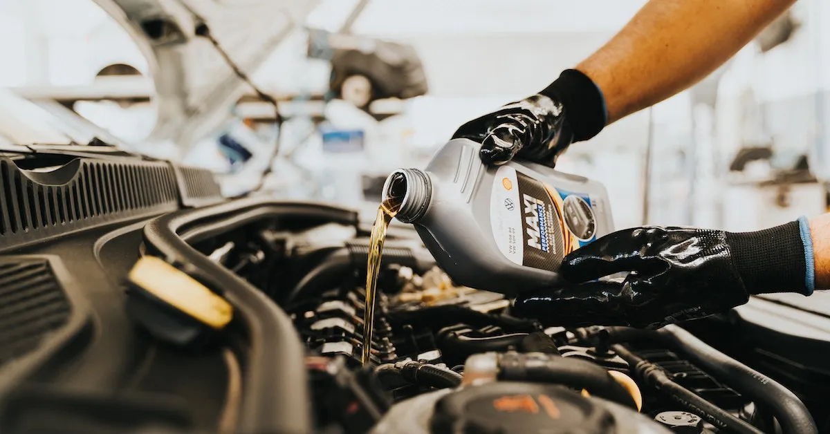 A mechanic wearing black rubber gloves pouring fresh engine oil into an engine after performing an oil change. Learn why oil changes on your vehicle are so important and some myths you need to learn about. Find the article here.