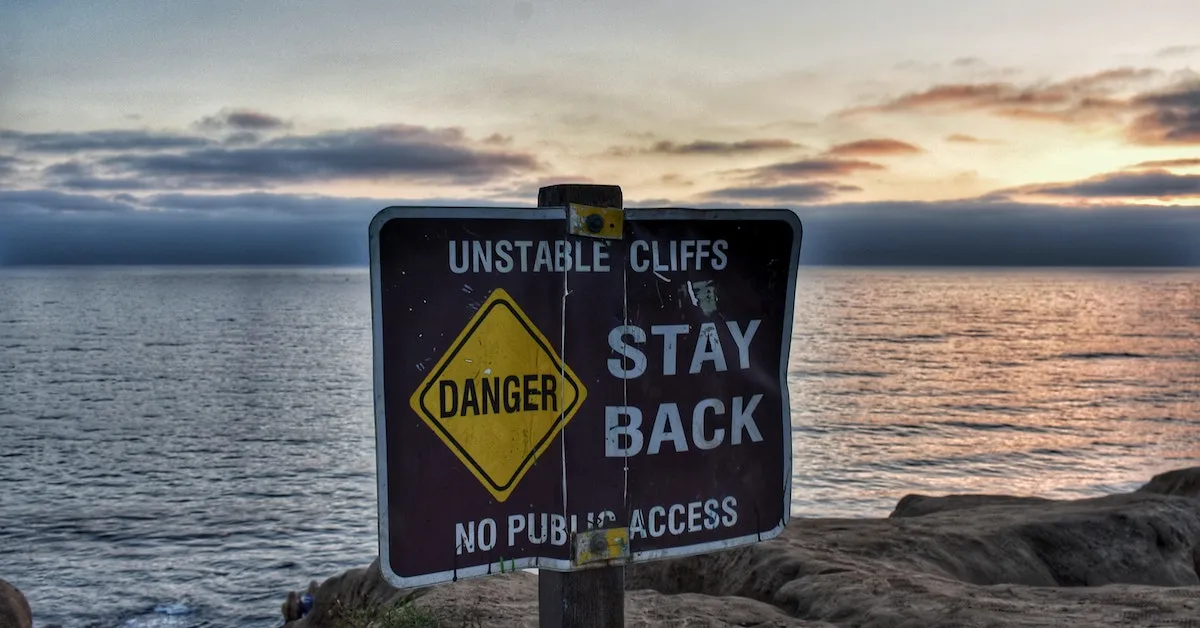 A sign in the foreground reads: Unstable Cliffs, Danger, Stay Back! Learn about the pitfalls of dating the wrong person. This article was written just for you!