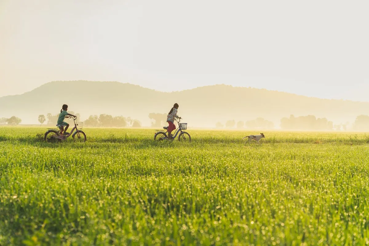 Two children riding bicycles through a large scenic field on a sunny day, with mountains in the background. The freedom and care-free life of a child reminds us how we should be as we pursue personal growth; for us to become filled with knowledge yet free to dream and as humble as a child. Learn more in our latest article.