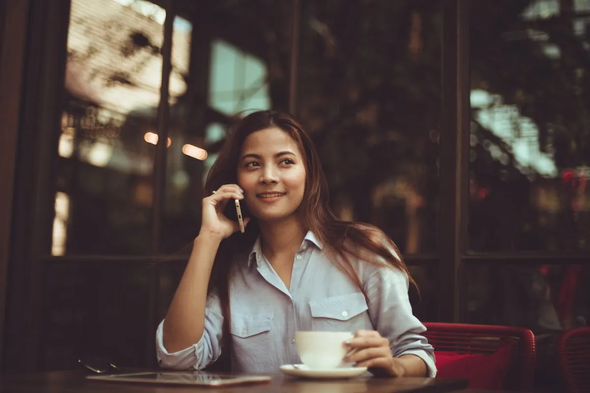 A woman sitting at an outdoor restaurant table talking on the phone and drinking coffee. She is smiling and aware that her words have a large impact on the conversation. Learn more about how the words we speak are very important in this new article from Ads4Dads.com