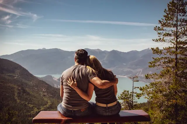 A married couple embracing while looking out into the distance of large mountains and a beautiful lake.