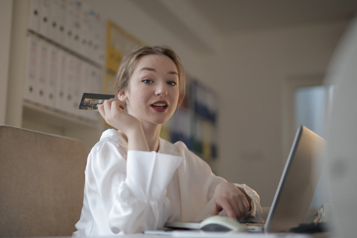 A young woman sitting in front of a laptop computer while holding a credit card.